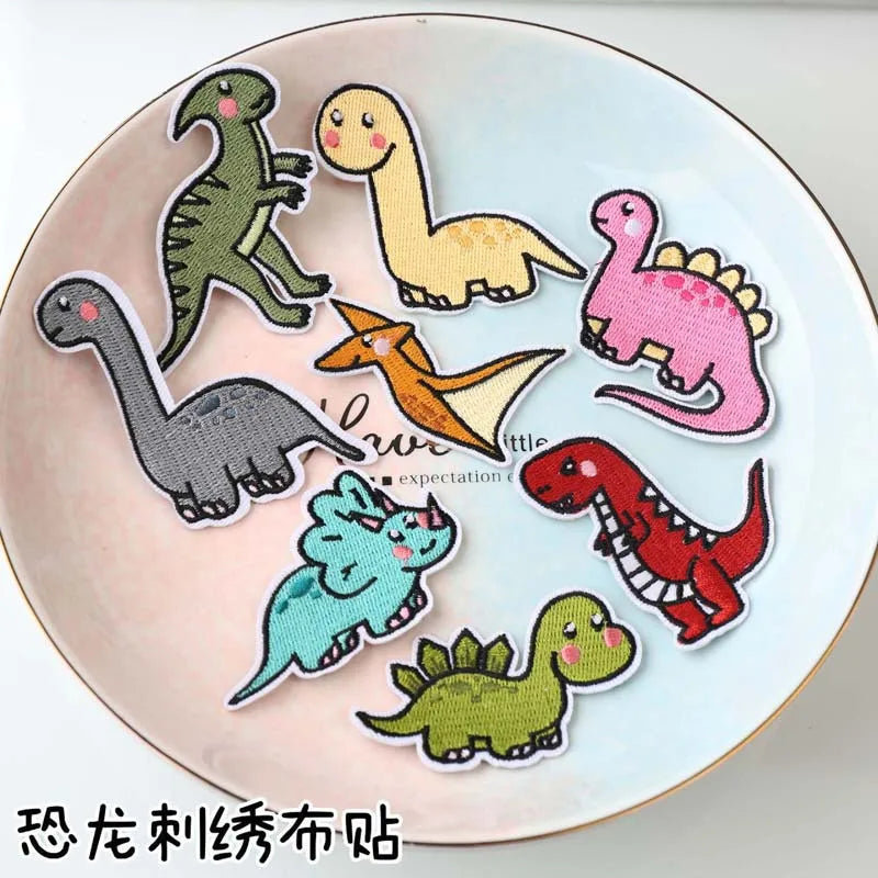 A set of iron-on patches featuring various dinosaur and animal figures on a light pink background.