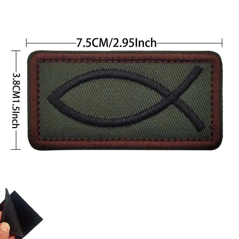 A rectangular olive green embroidered patch featuring a black cross and flag design.
