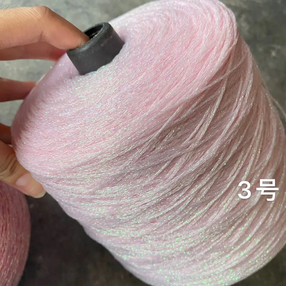 A skein of pink glitter metallic yarn is being held, showing the texture and color of the fiber.