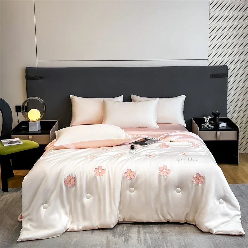 A light pink and white embroidered quilt is displayed on a bed with a dark gray headboard.