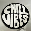 A round black floor mat with white fuzzy letters spelling out CHILL VIBES