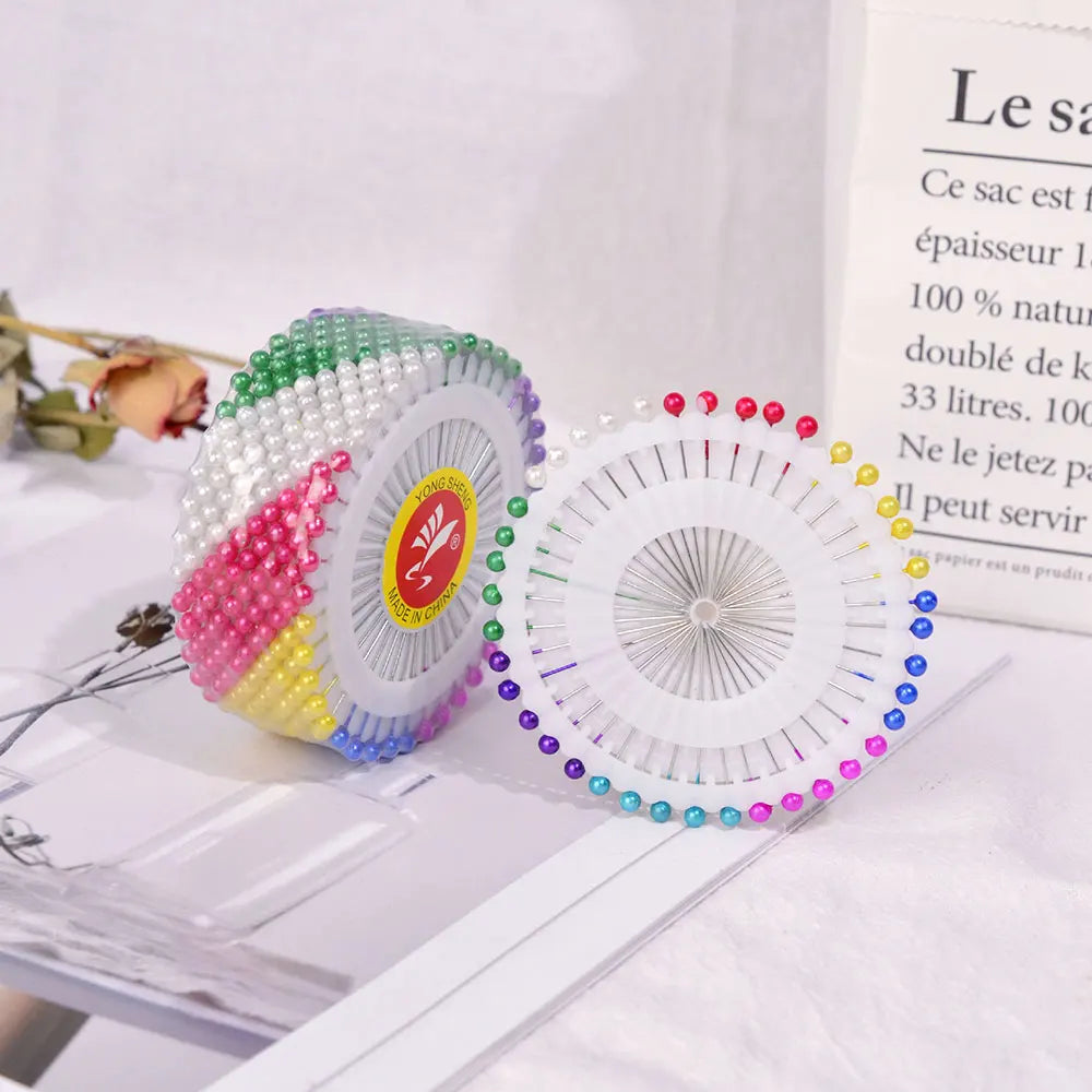 A set of pearl head pins for sewing and crafting displayed on a white surface.