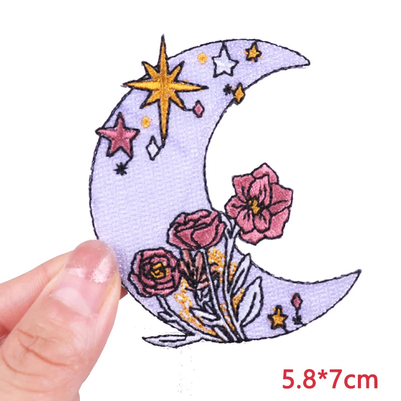 A purple crescent moon embroidered with yellow stars and pink flowers on a fabric patch.