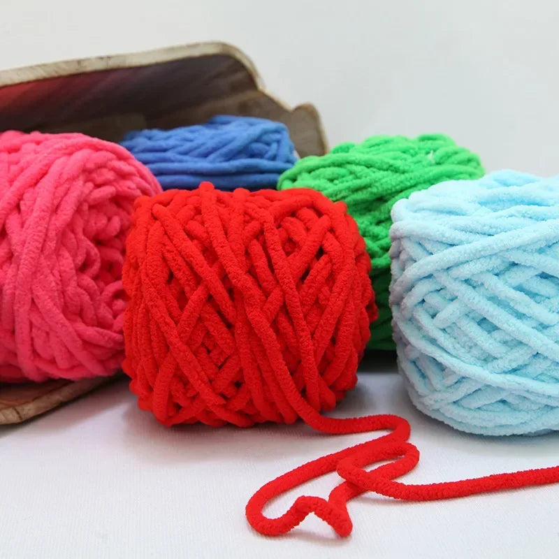 A pile of brightly colored chenille knitting yarn in red, blue, and green, with a loose strand extending from the pile.