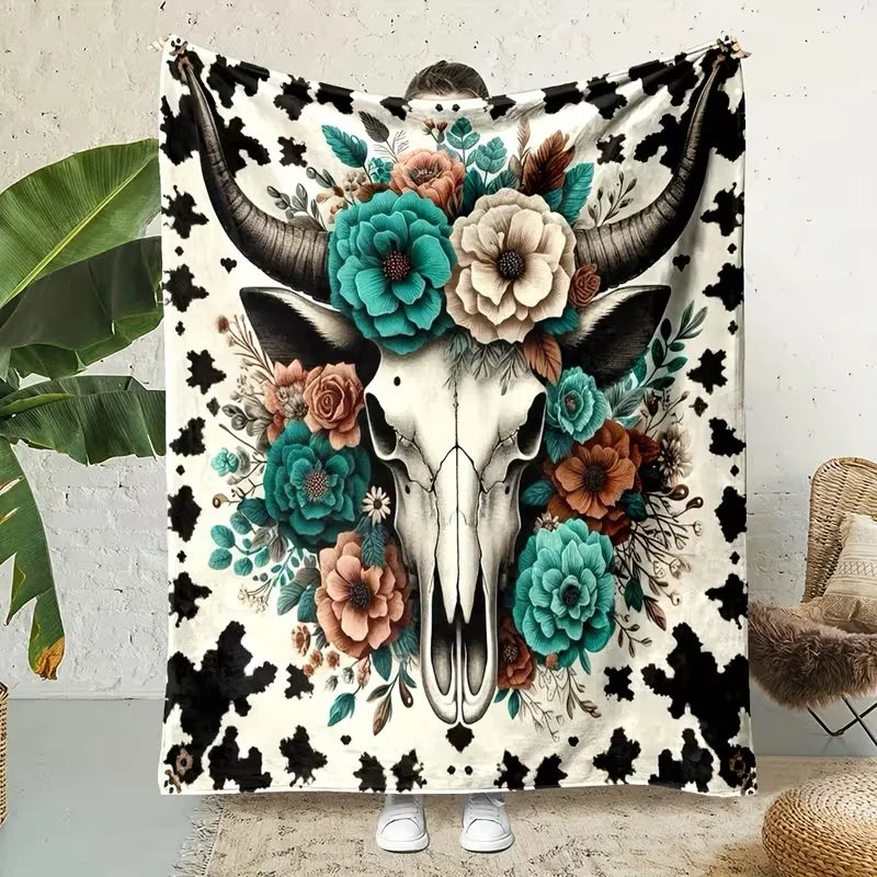 A flannel blanket featuring a detailed floral design of a Highland cow skull in shades of teal, brown, and cream on a black a