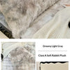 A fluffy light gray rabbit plush long pillowcase displayed on a bed with a white knitted blanket.