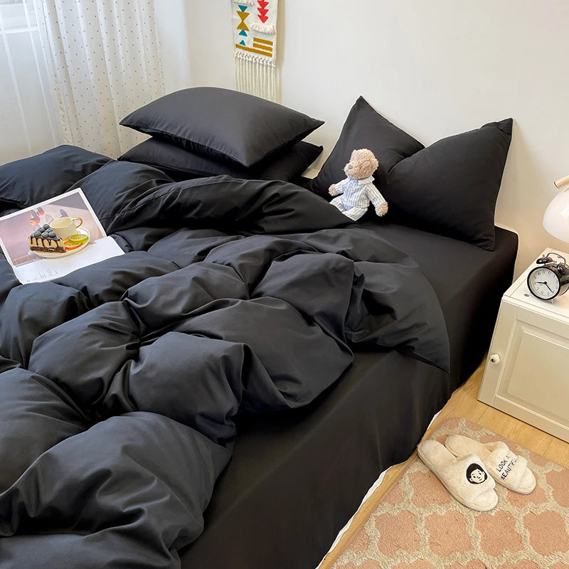 A black 3-piece duvet cover set with pillows and a small stuffed animal on a bed.