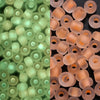 A close-up view of a 600-pack of 3mm glow-in-the-dark glass seed beads in various shades of green and pink.