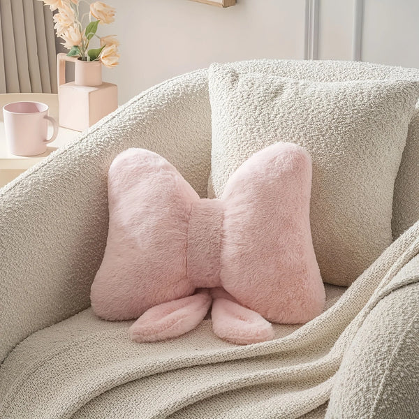 A pink fluffy decorative bow pillow resting on a beige knitted fabric sofa.