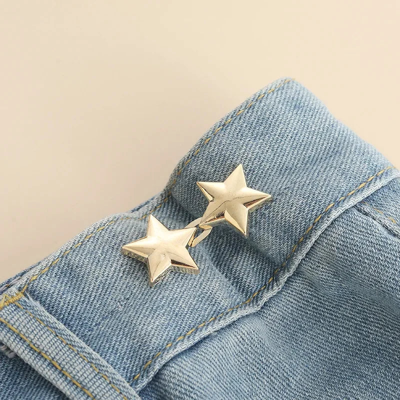 A pair of gold-toned star-shaped button clips attached to a blue denim fabric.