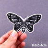 Black embroidered butterfly iron-on patch with intricate line work being held by a hand.