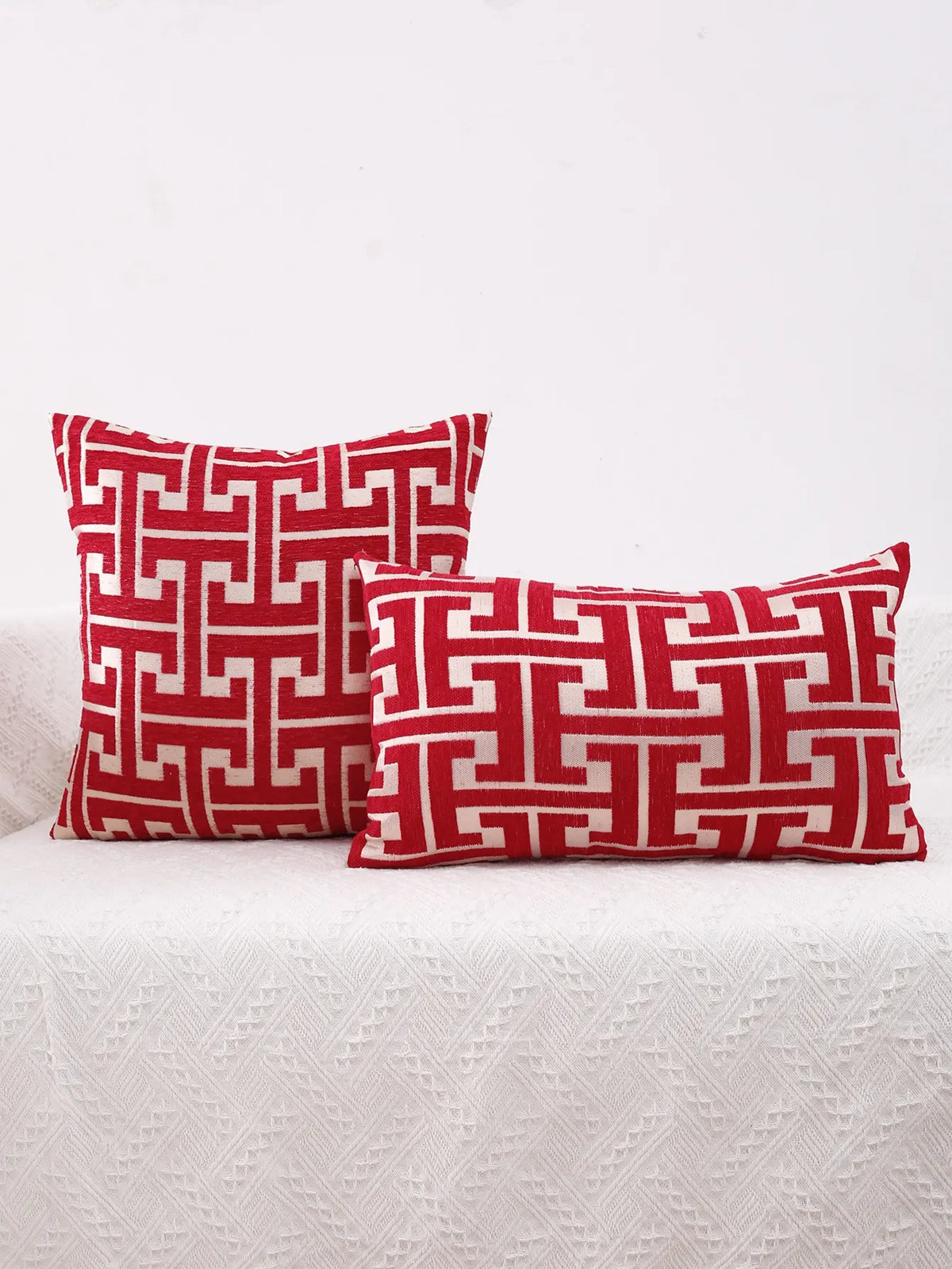 Two red and white geometric patterned throw pillows resting on a white textured fabric surface.