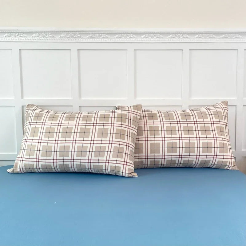 A set of two plaid patterned pillow covers resting on a light blue bed.