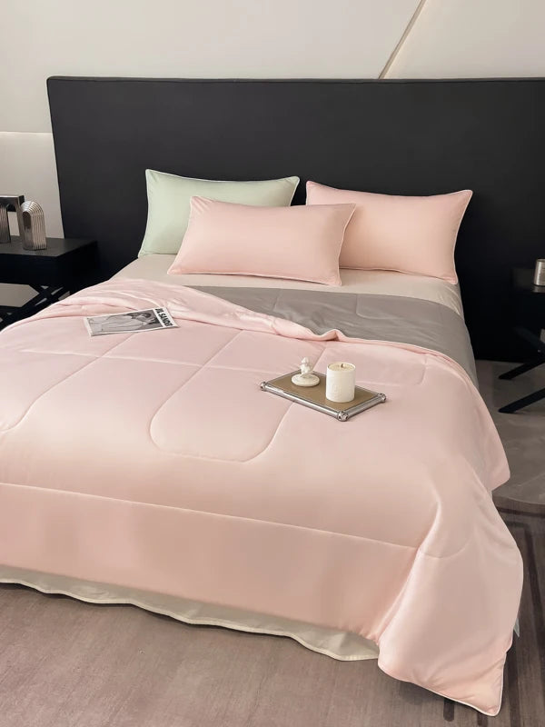 A pink reversible cooling quilt is displayed on a bed with gray bedding and light green pillows.