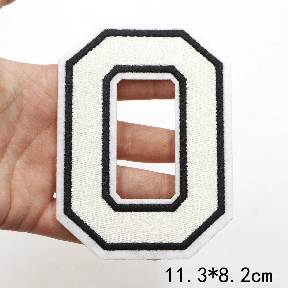A hand holds a white letter patch with a black border and an oval cutout, showing the size 11.3*8.2 cm.