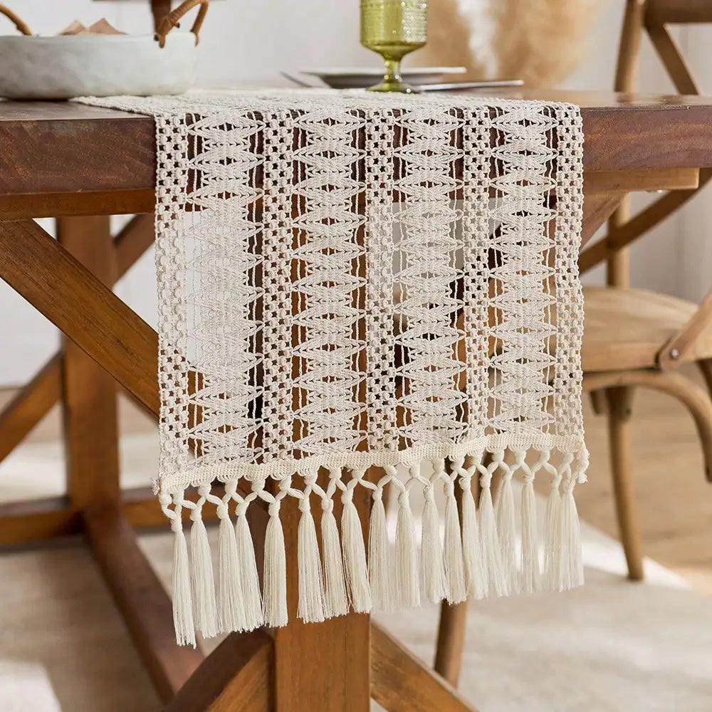 A cream crochet table runner with fringe details draped over a wooden table.