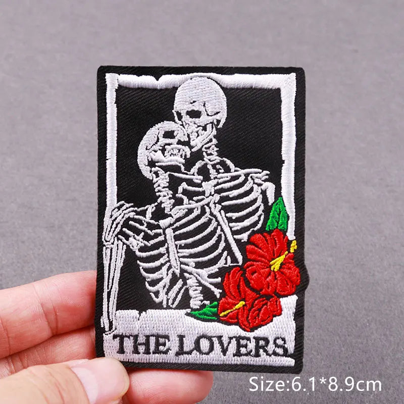 Black embroidered patch featuring two skulls and a red rose design.