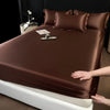 A close-up of a dark brown satin fitted sheet covering a mattress on a bed.
