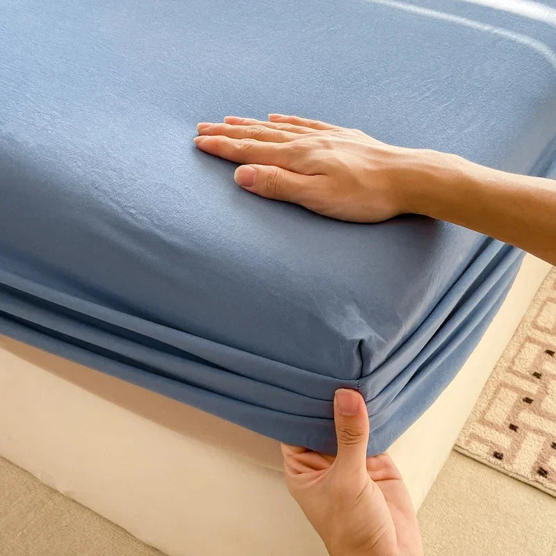 A hand is folding a blue fitted bed sheet made of premium 100% cotton.