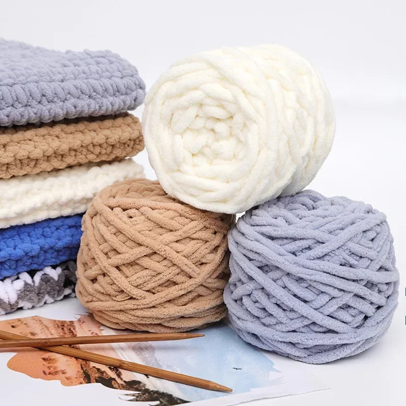 A pile of soft white, beige, and gray chenille knitting yarn balls with wooden chopsticks in the foreground.