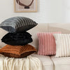 A stack of four plush decorative pillows in shades of gray, black, rust, and cream on a white sofa.