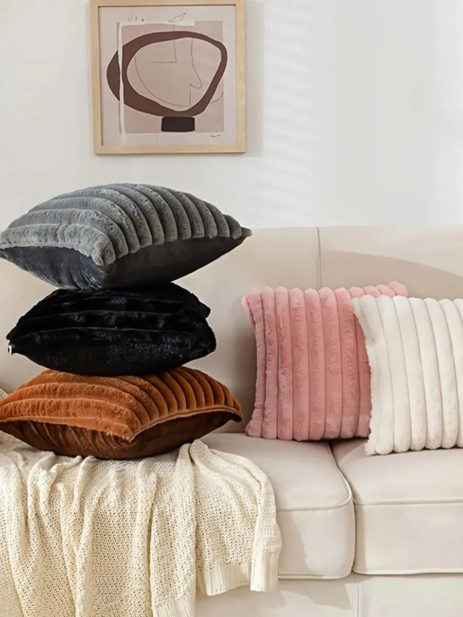 A stack of four plush decorative pillows in shades of gray, black, rust, and cream on a white sofa.