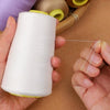 A hand is unwinding a spool of white polyester sewing thread onto a thin strand.