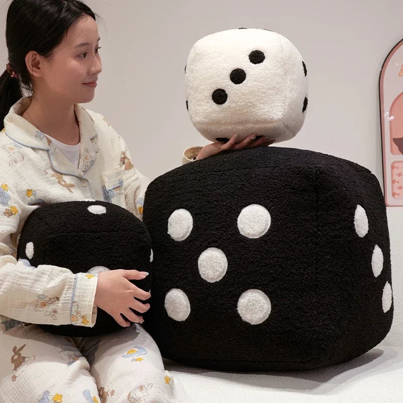 A person is holding two oversized black and white polka dot dice plush pillows.