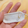 A hand holds a white, gourd-shaped locking safety pin for knitting and sewing.