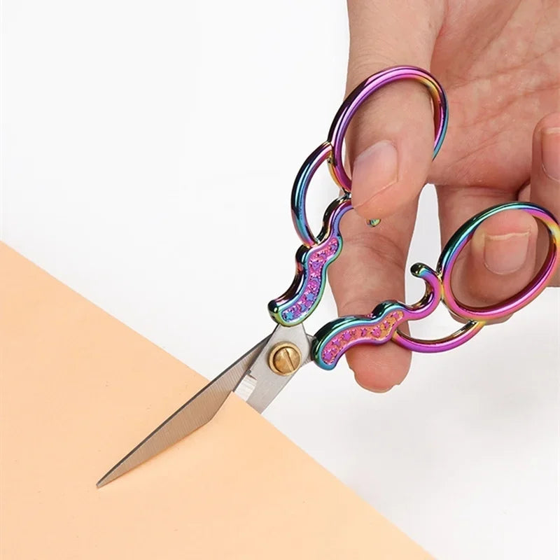 A hand holds a pair of vintage stainless steel sewing scissors with colorful handles and a silver blade.