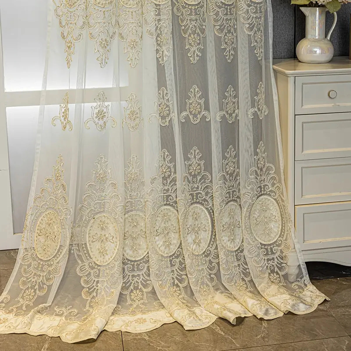 A sheer, ivory embroidered beaded curtain with a punched-hole design hanging in a window.