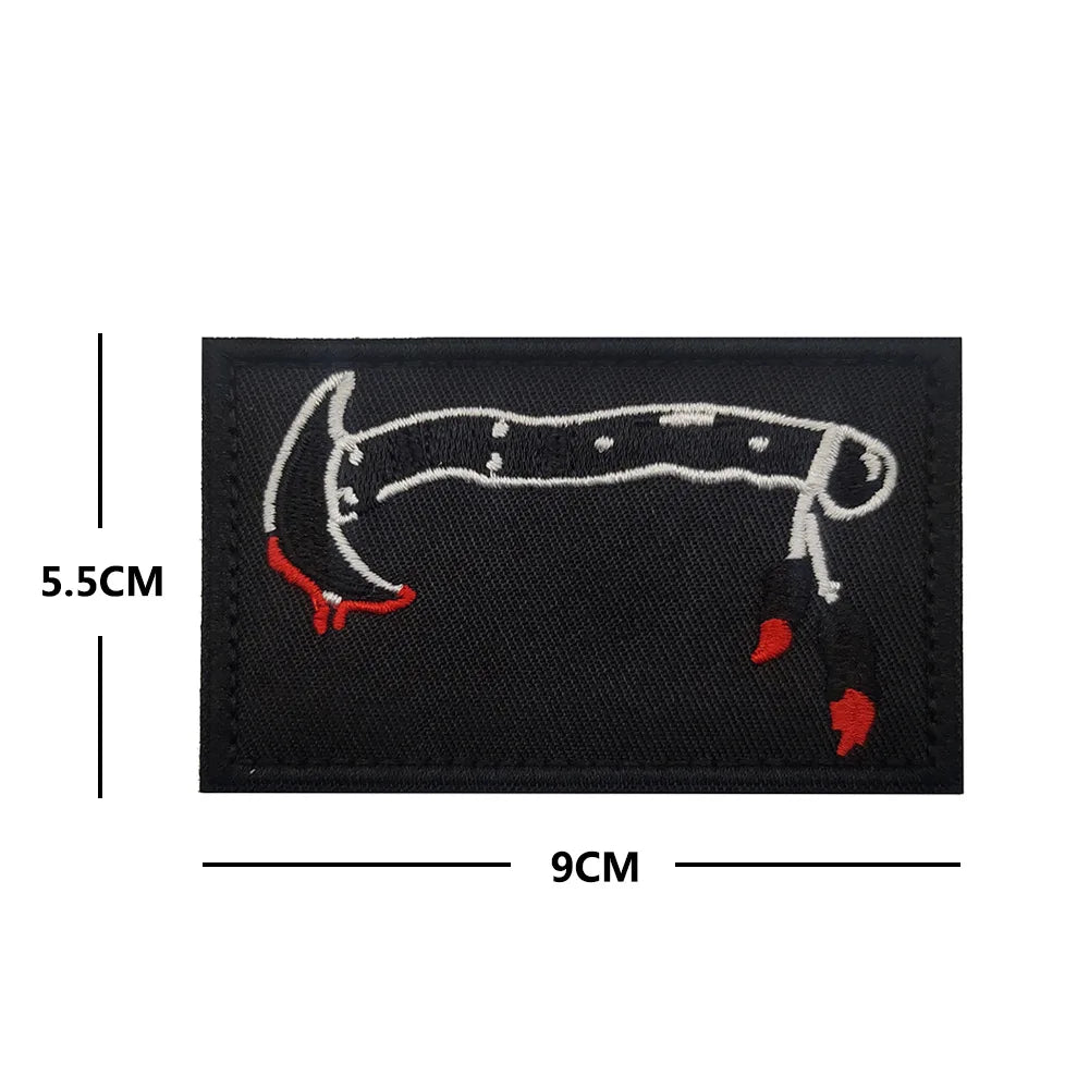 A black embroidered patch featuring a white outline of a skull and crossbones with red accents.