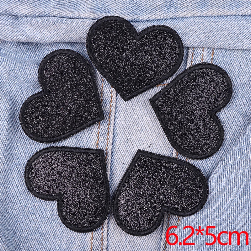 Five black glitter iron-on embroidered love heart star patches arranged in a circle on denim fabric.