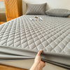 A gray waterproof mattress protector fitted sheet is displayed on a bed, folded over the edge.