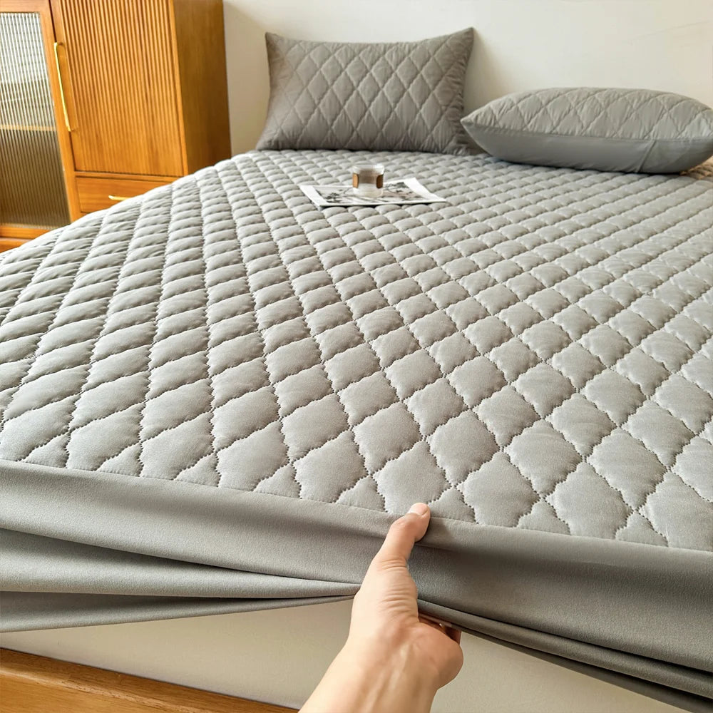 A gray waterproof mattress protector fitted sheet is displayed on a bed, folded over the edge.