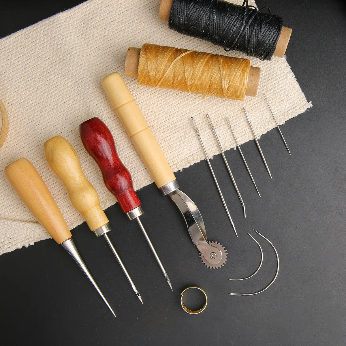 A leather craft sewing kit showing waxed thread, a spool of thread, and various needles and tools on a beige cloth.