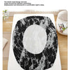 A black and white marble print fitted sheet is shown on a bed, emphasizing its secure elastic band design.
