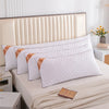 A set of white rectangular sleeping pillows with subtle orange accents resting on a bed.