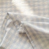 A close-up of a light gray organic cotton flat sheet showing a subtle plaid pattern.