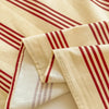 A close-up of beige organic cotton bedding featuring red stripes on a flat sheet and pillowcases.