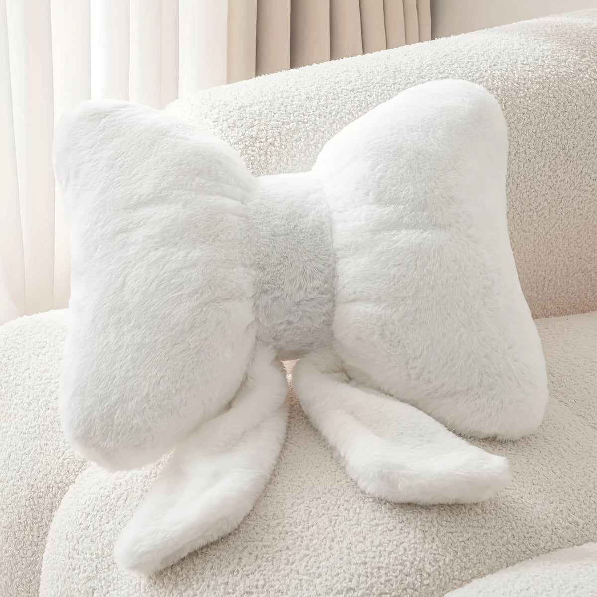 A fluffy white decorative bow pillow resting on a light-colored sofa.