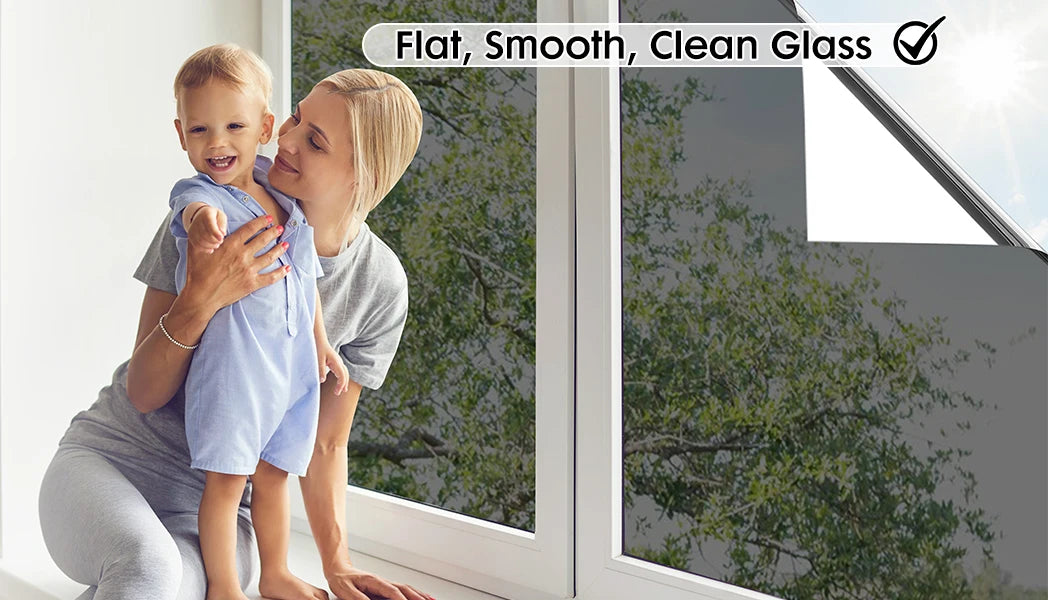 A mother holds a child in front of a window with clear glass, demonstrating the flat, smooth finish of privacy film.