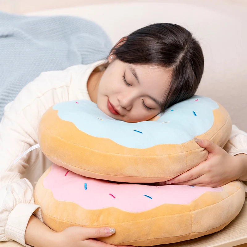A person is hugging a soft, round plush pillow shaped like a fried doughnut in pink and orange colors.