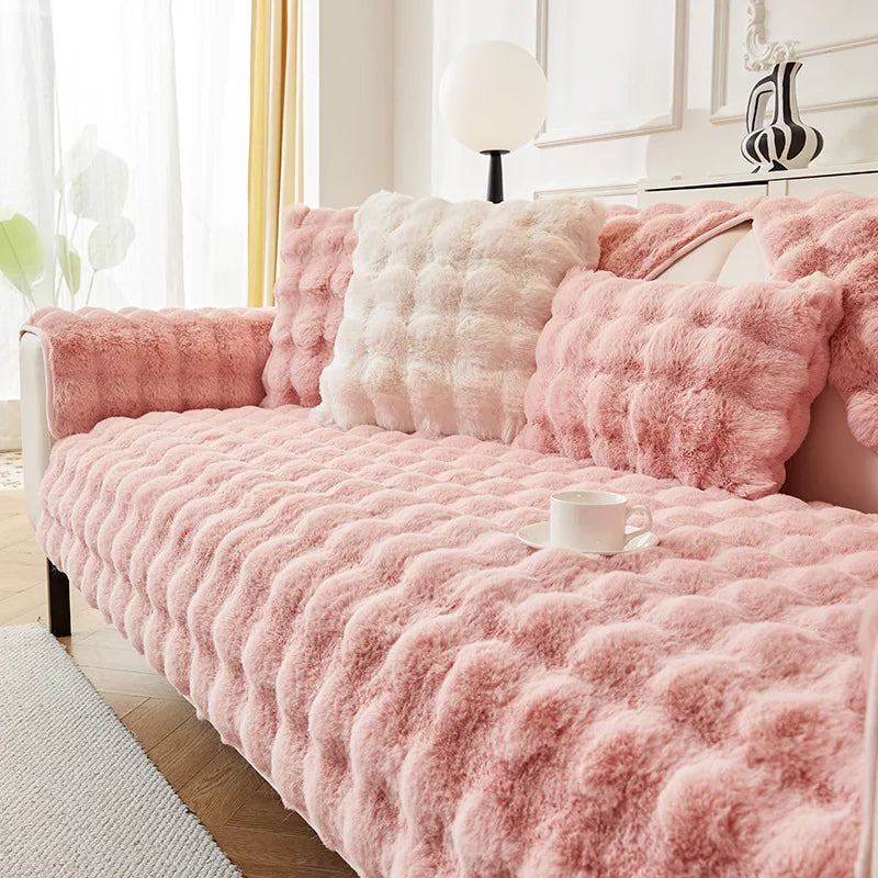 A pink plush rabbit fur sofa cushion cover draped over a light pink sofa in a bright room.