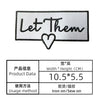 A rectangular white embroidered patch with black text that reads Let Them