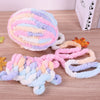 A ball of multi-colored, fluffy yarn in pink, purple, and blue is displayed next to a skein of yarn on a wooden surface.