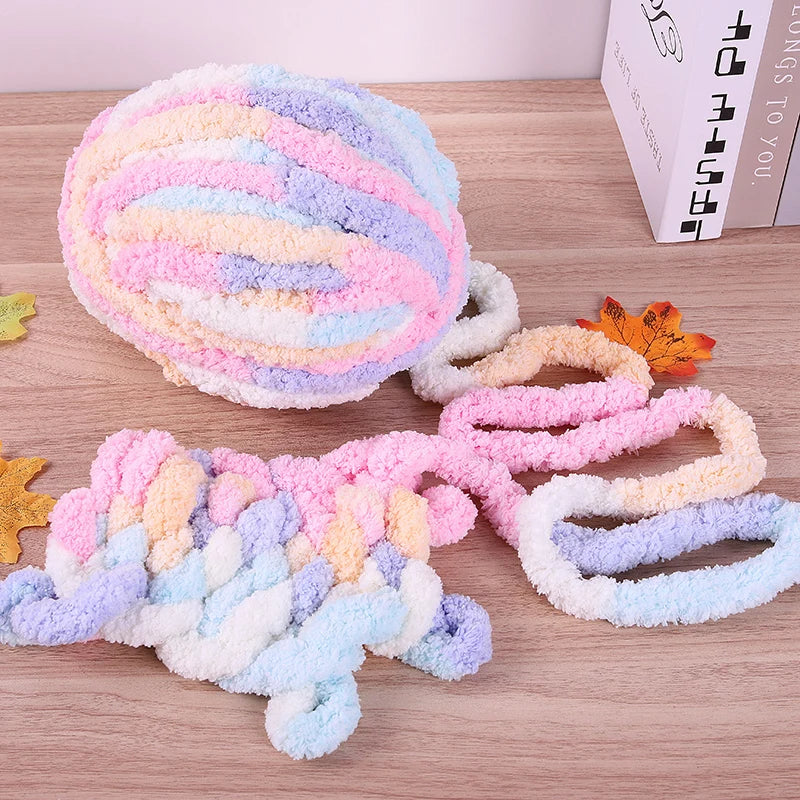 A ball of multi-colored, fluffy yarn in pink, purple, and blue is displayed next to a skein of yarn on a wooden surface.