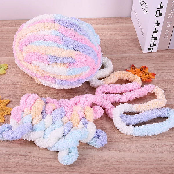 A ball of multi-colored, fluffy yarn in pink, purple, and blue is displayed next to a skein of yarn on a wooden surface.