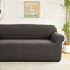 A dark gray sofa slipcover featuring a jacquard leaves pattern, placed in a bright room.