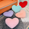 A collection of heart-shaped plush cushions in pink, red, light blue, and purple resting on a gray patterned surface.